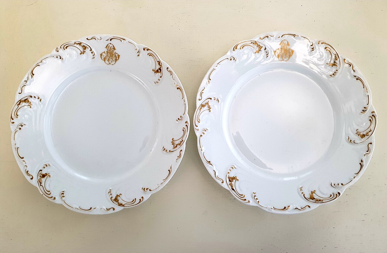 Two antique Limoges porcelain plates with scalloped gilt scroll rims and a gold monogram at the top
